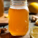 homemade kombucha recipe in a glass jar with a visible SCOBY on a wooden kitchen counter